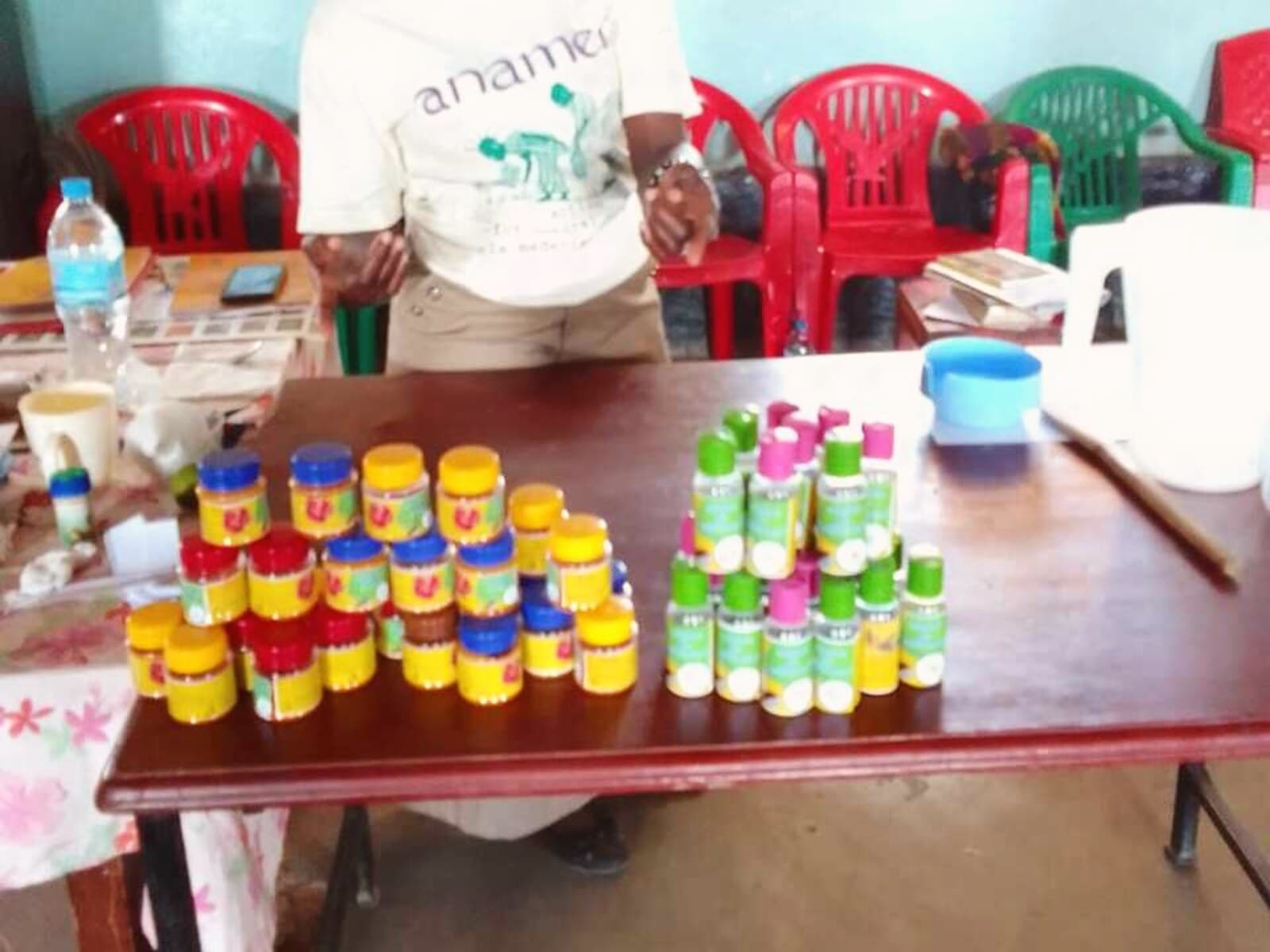 Flora Luferano im anamed-T-Shirt hinter einem Tisch voller selbst hergestellter Heilsalben-Tiegel und Tinkturfläschchen in Mwanza